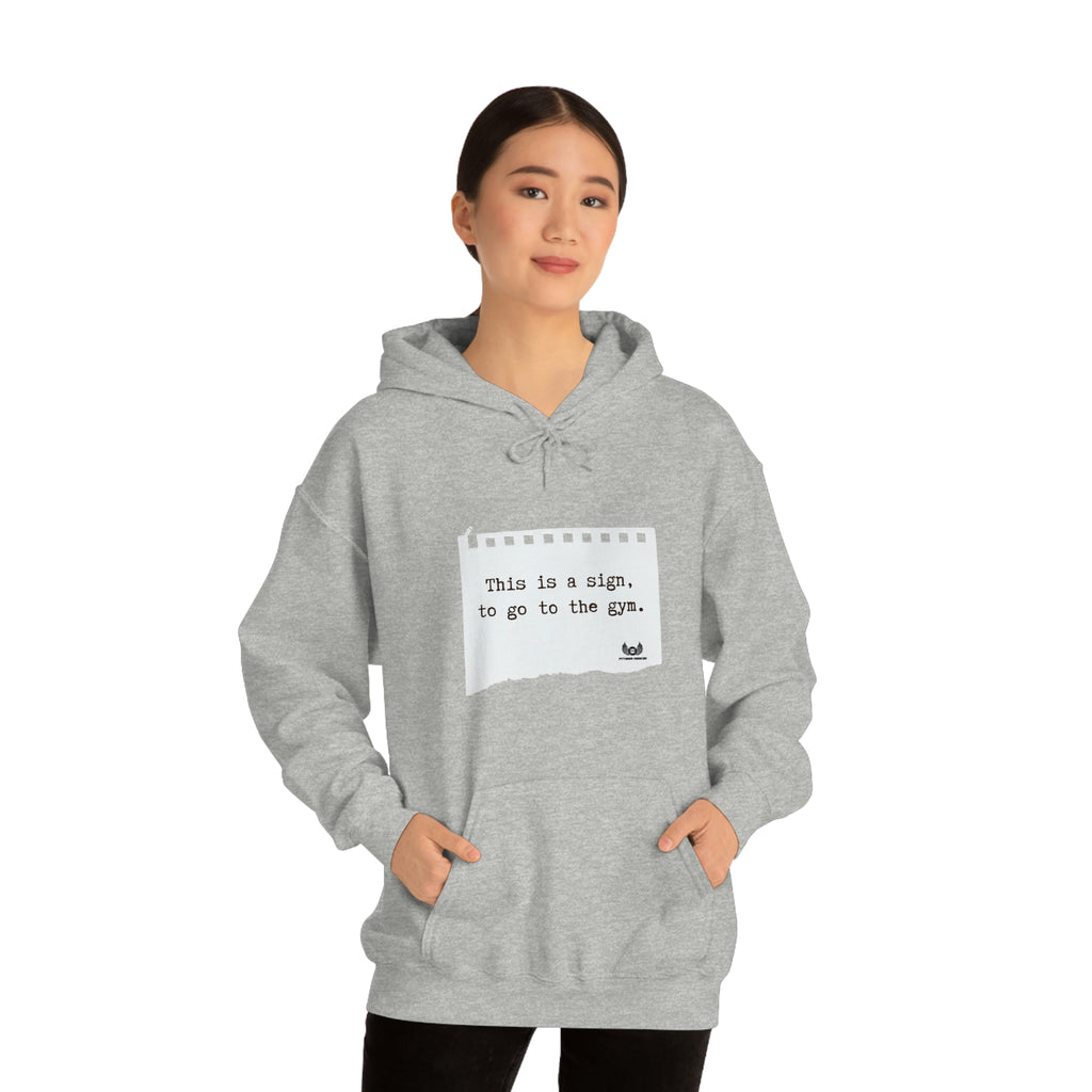 Picture of the Fitness Geeker graphic saying "This is a sign, to go to the Gym" Heavy Blend Hooded Sweatshirt (front) in grey model